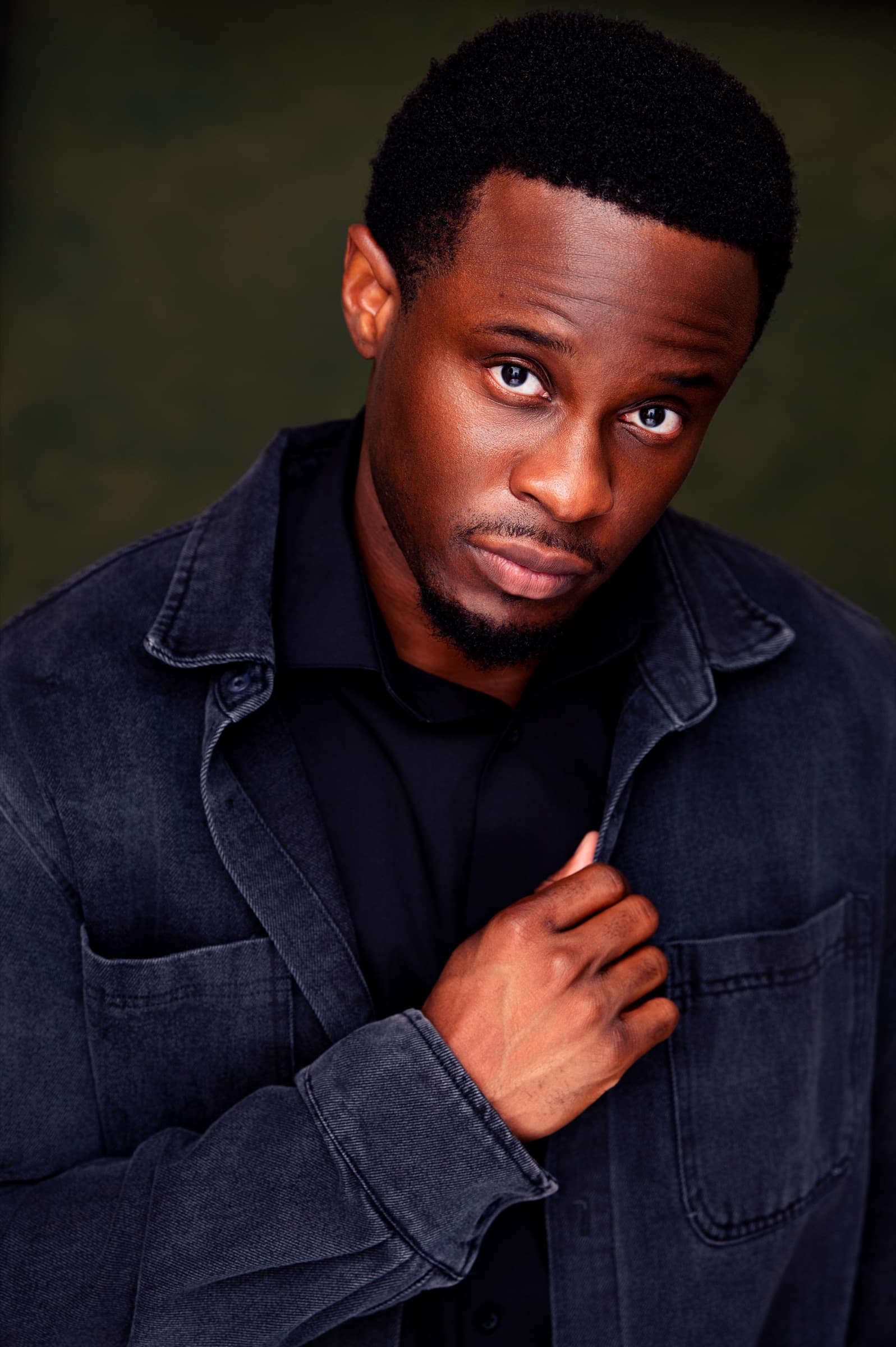 Lanre Adigun headshot — denim jacket, olive backdrop